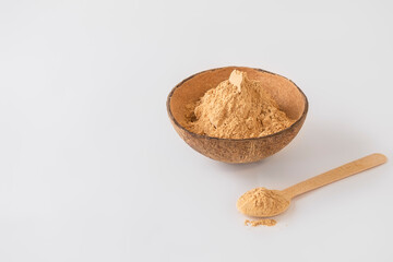 Bowl of maca root powder with spoon on white background