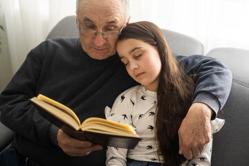 Book, family and children with a girl reading to her grandfather on the floor of their living at home. Kids, read and story with a senior man and granddaughter bonding in their house during a visit.