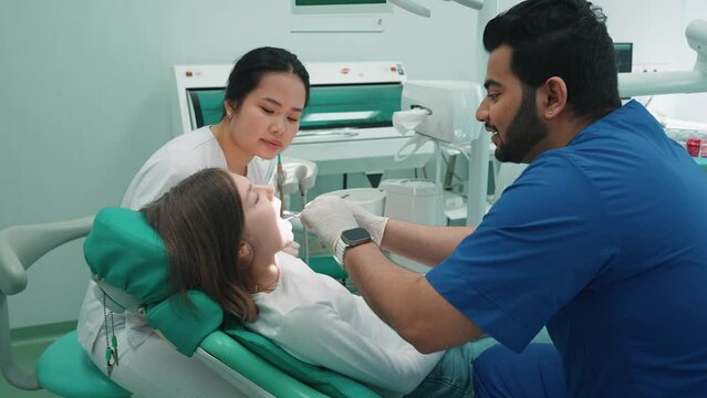 Friendly indian dentist man checking patient oral cavity with mirror in hospital. Dentist appointment