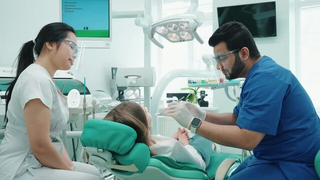 Happy indian dentist man examining patient oral cavity with mirror in hospital. Dentist appointment