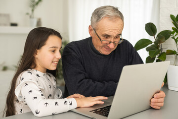 Happy retirement grandfather and pretty granddaughter laughing while watching e-book for learning...
