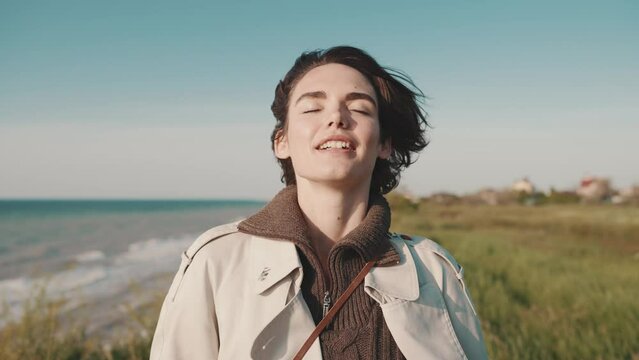 Relaxed woman breathing with closed eyes while standing on field near sea