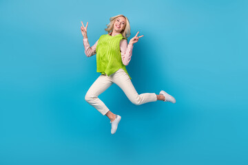 Fototapeta na wymiar Full body photo of pretty overjoyed lady jumping demonstrate v-sign isolated on blue color background