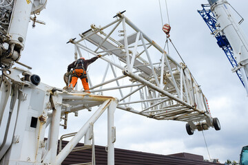 worker in hard hat and hi-vis guides jib extension for 1000 ton mobile crane into position