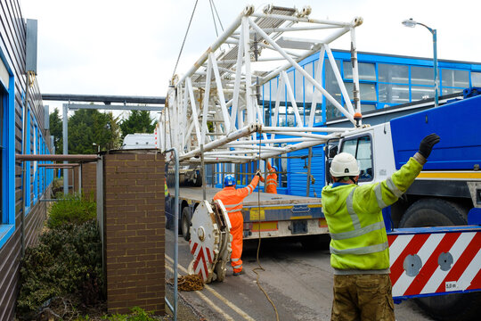 workers in hi-vis and hard hats guide lift of 1000 ton mobile crane jib off truck flatbed