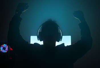 Man in dark room, silhouette with video game and winning, fist pump and online streaming with...