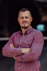 A successful young businessman in a shirt, with crossed arms, poses outdoors, confident expression on his face.