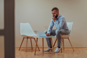 A confident businessman sitting and using laptop with a determined expression, while a beige background enhances the professional atmosphere, showcasing his productivity and expertise.