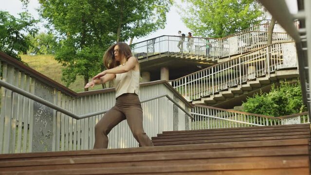 Beautiful Caucasian girl dancing on the street. A smiling woman on the stairs performs dance moves. Urban lifestyle concept of smiles. High quality 4k footage
