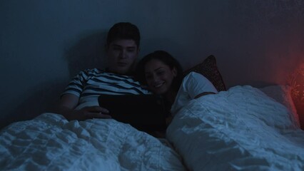 Young couple cuddles up in bed watching a tablet device at night - Powered by Adobe