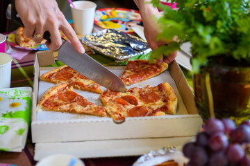 A hand cuts pizzas on the table. Festive bright fast food.