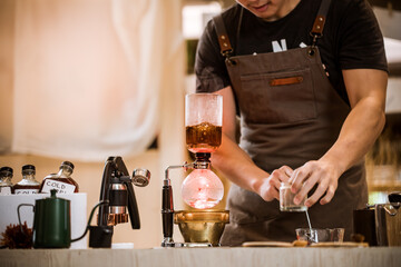 Professional coffee maker - Barista using coffee siphon brewing hot espresso at coffee shop coffee brewing syphon alternative method. Startup Business Concept.