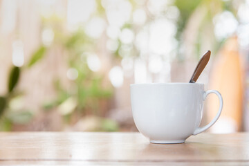 A morning cup of coffee on a wooden table with blurry bokeh from the trees in the background.