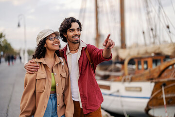 A cheerful couple on a dock is hugging and pointing at city sights during their trip to Spain.