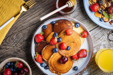 American pancakes with blueberries, strawberries and cherries with dip of honey. Placed on a rustic designer plate, on wooden rustic board. 