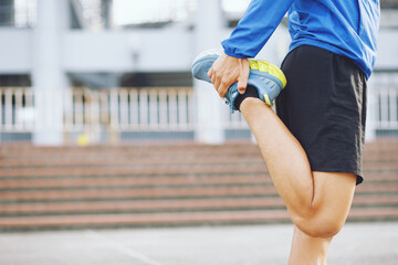 young man runner stretching for warming up before running or working out on the road. Track and Field Athlete exercise. Fitness and sport healthy lifestyle concept. copy space banner.