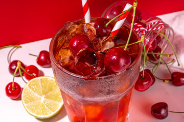Iced cherry cola drink, Cold summer fruity non-alcohol cocktail with fresh cherries, juice, cola and ice, on high-colored background copy space