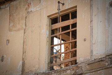 Old window with metal trellis outside abandoned aged house with visible open window on the opposite wall of the room