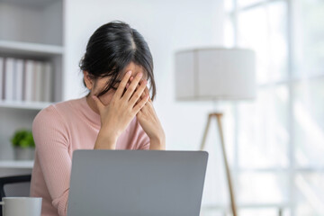 Confused and stressed Asian businesswoman looking at her laptop screen, pensively thinking of a plan to solve the problems, working in her office.