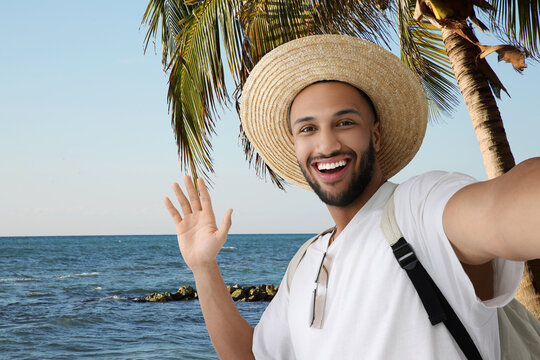 Smiling young man in straw hat taking selfie at tropical resort