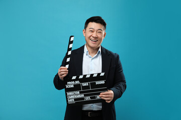 Happy asian actor with clapperboard on light blue background. Film industry