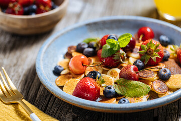 Small American pancakes mixed with seasonal fruit like strawberries, blueberries and cherries. Dipped with melted chocolate, placed on a rustic wooden board. 