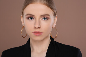 Beautiful young woman with elegant earrings on light brown background