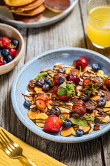 Small American pancakes mixed with seasonal fruit like strawberries, blueberries and cherries. Dipped with melted chocolate, placed on a rustic wooden board. 
