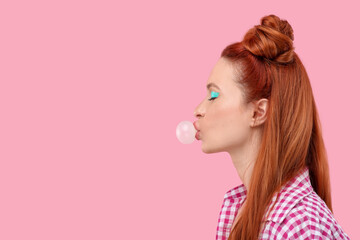 Beautiful woman with bright makeup blowing bubble gum on pink background. Space for text
