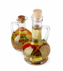 Glass jugs of cooking oils with spices and herbs on white background