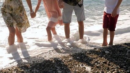 A happy family with children is walking along the seashore at sunset, the waves are hitting their legs. Legs close-up. 