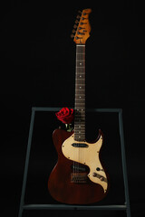 Beautiful rose near electric guitar on black background