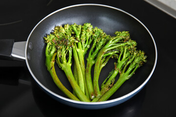 Frying pan with tasty cooked broccolini on cooktop, closeup