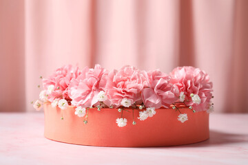 Fototapeta na wymiar Orange round stand, gypsophila and carnation flowers on pink marble table, closeup. Stylish presentation for product