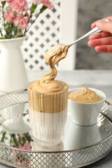 Woman pouring cream for dalgona coffee into glass at table, closeup