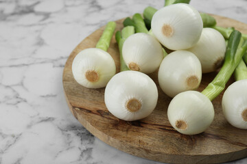 Wooden board with green spring onions on white marble table, closeup. Space for text