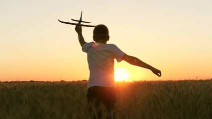 boy teenager child kid runs through field with wheat with toy plane his hands sunset, happy dream...