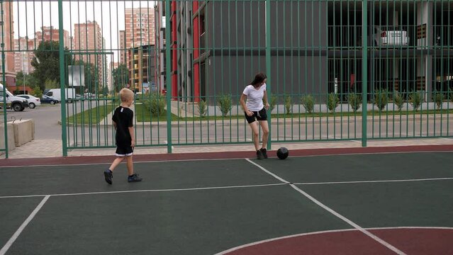 A happy mother is playing soccer with her child on the playground in the courtyard of a modern residential complex.