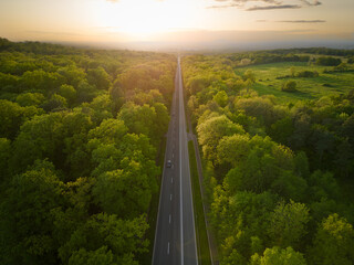high angle view of a straight road going through the forest at sunset - obrazy, fototapety, plakaty