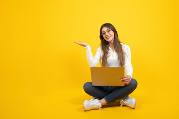 Woman holding open palm, demonstrate offer advertising template copy space ad, banner design concept idea. Cheerful caucasian girl sitting on the ground with laptop.  Isolated over yellow background. 