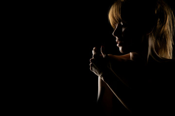 Fototapeta na wymiar Silhouette of a young woman touching her shoulder on a black background