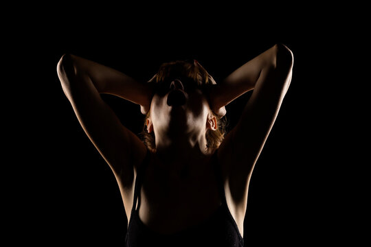 Portrait of a screaming woman in the shadow, hold her head , closed eyes on a black background