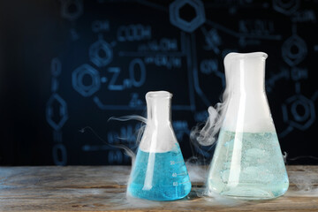 Laboratory glassware with colorful liquids and steam on wooden table against black background,...