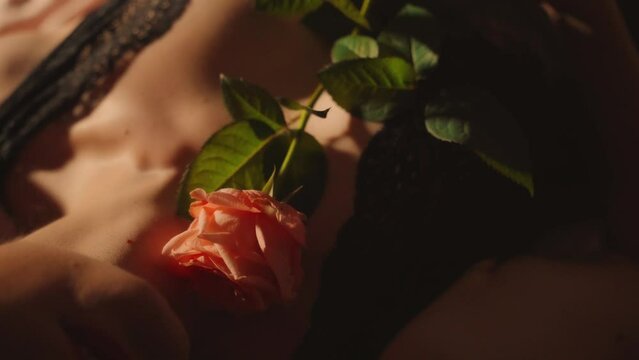 Closeup portrait sexy woman touching herself stroking skin breasts seductive body lingerie with pink rose flower. Adult girl in black lace underwear lies on bed face is cropped red lips. fashion model