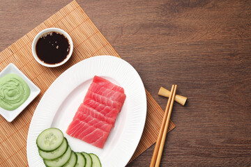 Tasty sashimi (pieces of fresh raw tuna), cucumber slices, soy sauce and wasabi on wooden table,...