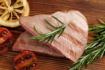 Pieces of delicious tuna steak with rosemary, tomato and lemon on wooden board, closeup