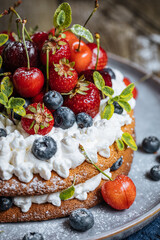 Fresh seasonal layered cake with spring ripe fruit like strawberries, blueberries and cherries. Placed on a elegant blue plate on rustic wooden board