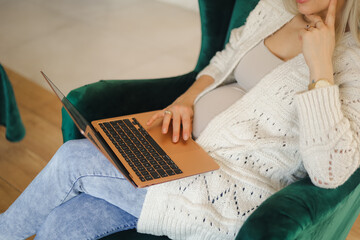 Cropped image of pregnant woman working on a laptop while sitting in armchair at home