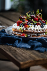 Fresh seasonal layered cake with spring ripe fruit like strawberries, blueberries and cherries. Placed on a elegant blue plate on rustic wooden board