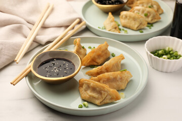 Delicious gyoza (asian dumplings) with soy sauce, green onions and chopsticks on white table